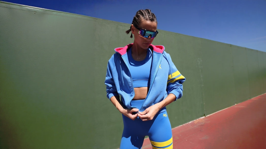 Woman resting in a blue high-waisted leggings and bicolor blue pink hoodie jacket after a work out.  Premium women's running apparel by One More Reason crafted in Europe.