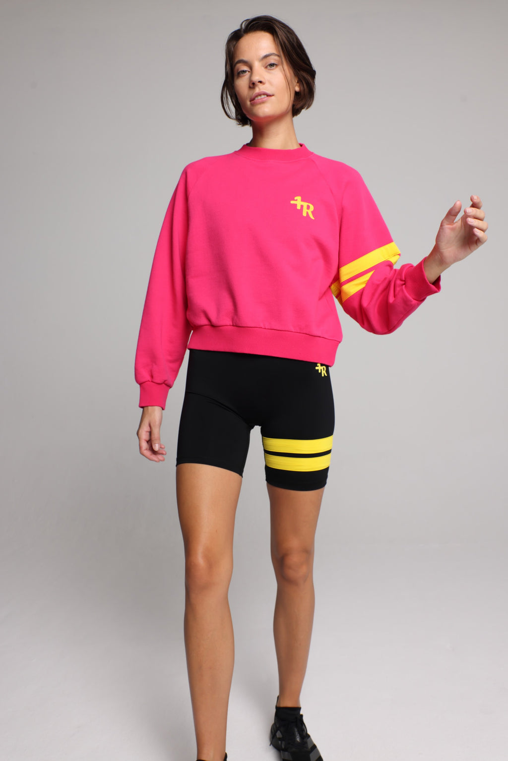 woman wearing premium pink organic crew sweater and black performance shorts with yellow stripes by One More Reason, women's luxury activewear indoor set