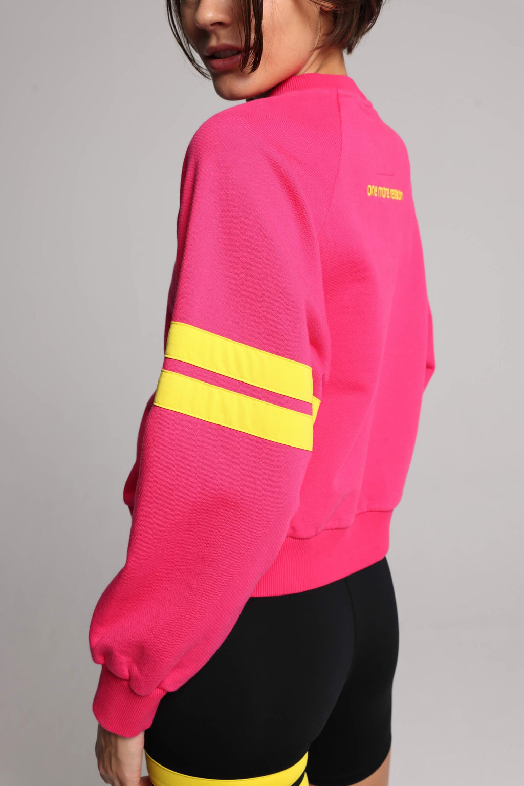 woman wearing premium pink organic crew sweater and black performance shorts with yellow stripes by One More Reason, women's luxury activewear indoor set