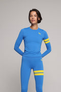 Woman wearing a premium blue long-sleeve sports top and blue leggings with yellow stripes by One More Reason fashion forward luxury sports wear 