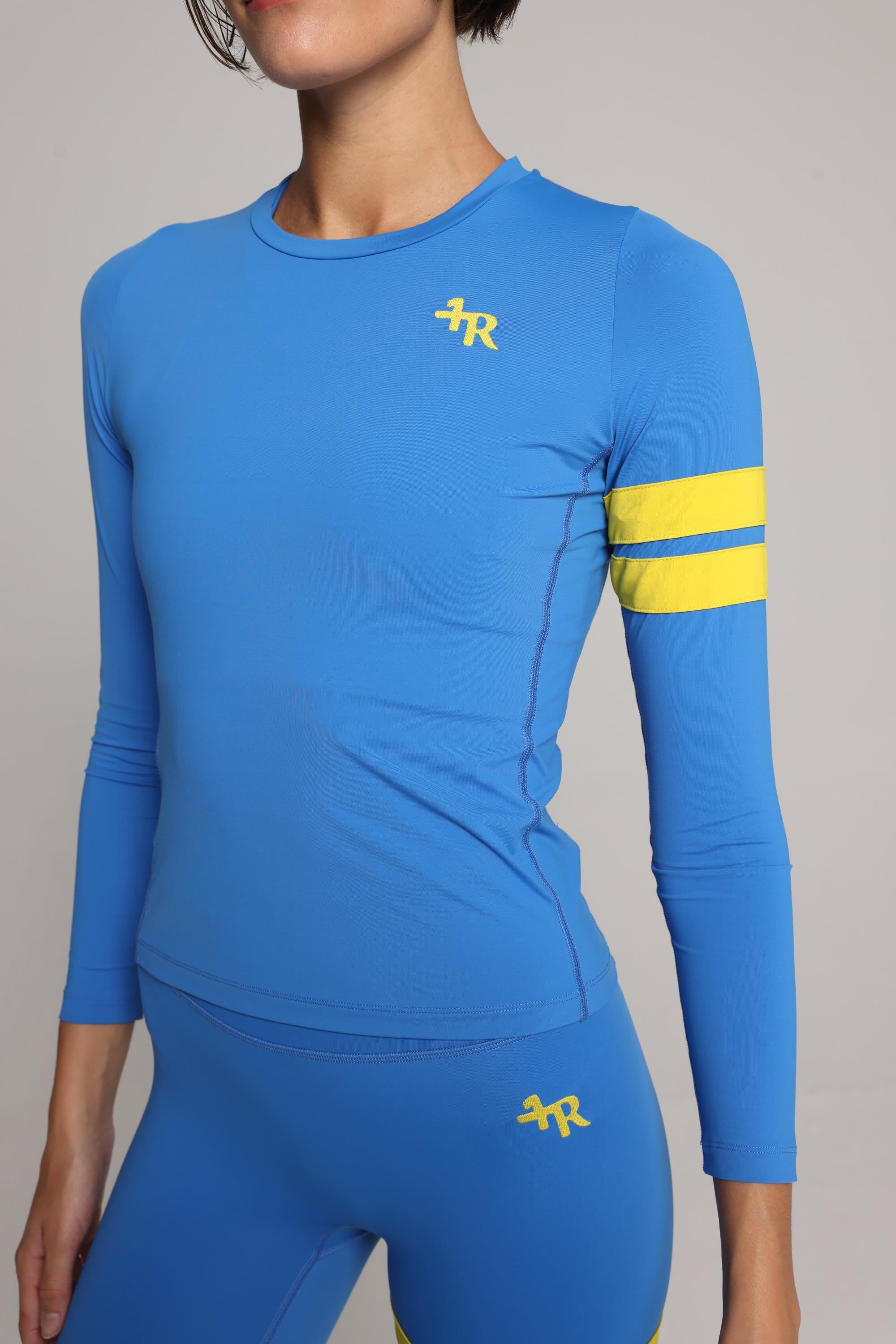 Woman wearing a premium blue long-sleeve sports top with yellow stripes by One More Reason fashion forward luxury sports wear 