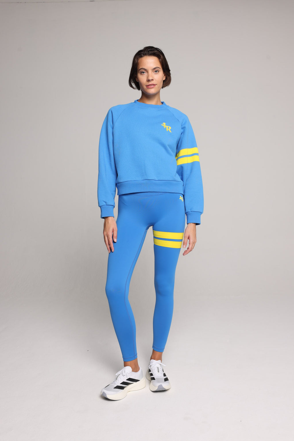 Woman wearing blue high-waisted leggings and oversized  blue crew sweater with yellow stripes by One More Reason, studio shot.
