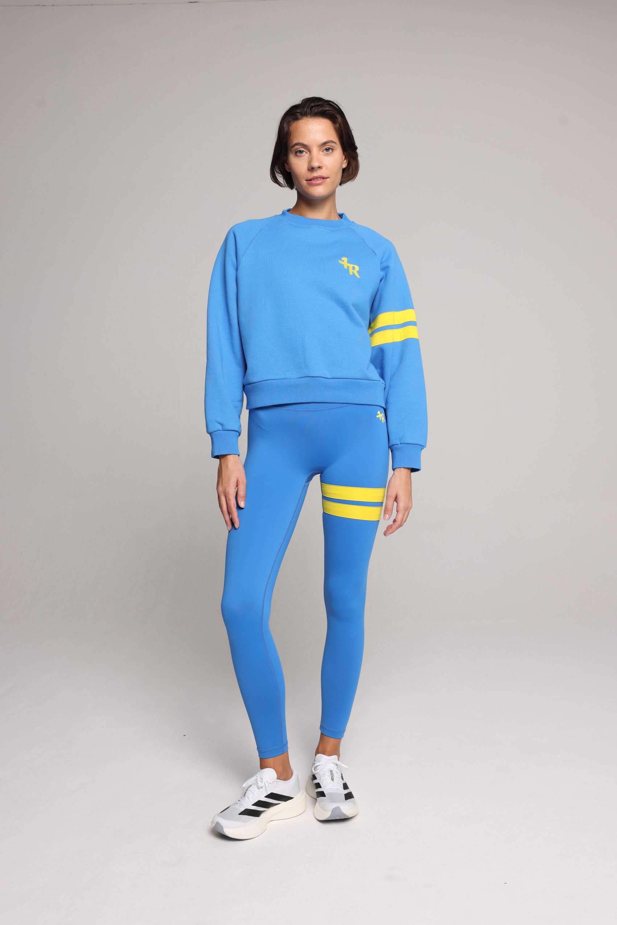 Woman wearing blue high-waisted leggings and oversized  blue crew sweater with yellow stripes by One More Reason, studio shot.