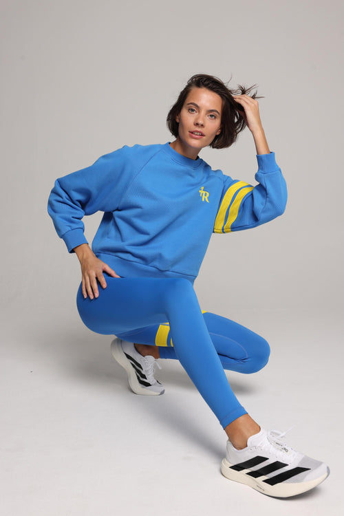 Woman wearing blue high-waisted leggings and oversized  blue crew sweater with yellow stripes by One More Reason, studio fashion.