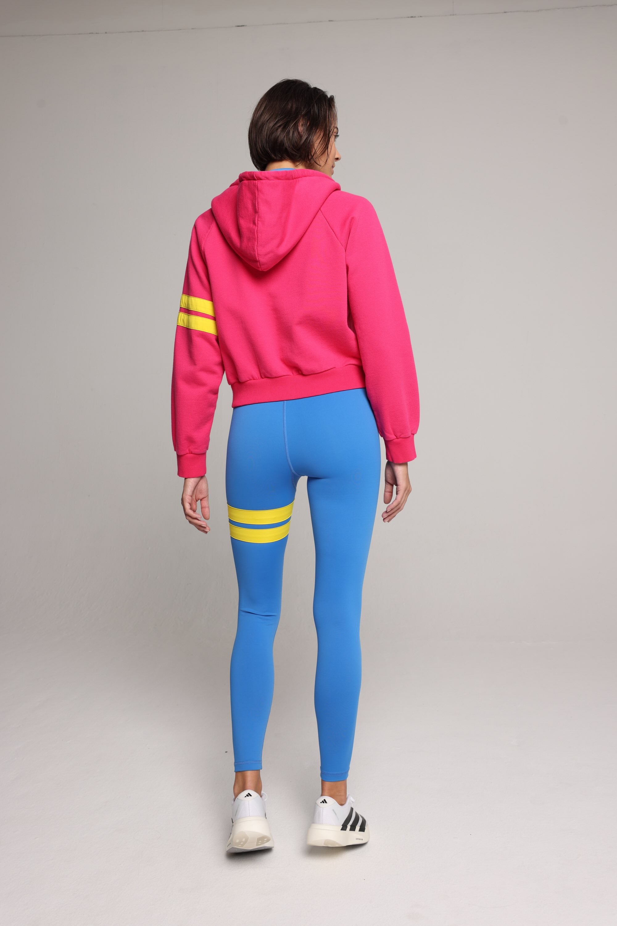 woman wearing bicolor organic cotton zip hoodie in pink and blue and blue tights  with yellow stripes by One More Reason, women's luxury activewear indoor set back view