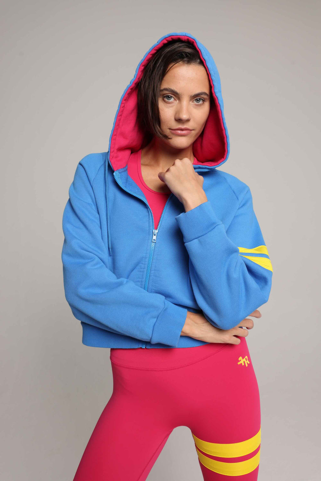 Women wearing blue and pink luxury athletic set, blue bicolor zip hoodie and pink tights by  One More Reason, with yellow stripes, studio look.