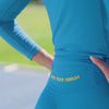 Female athlete running in a stadium wearing sky sportswear, leggings and long sleeve top, both with yellow stripes. 