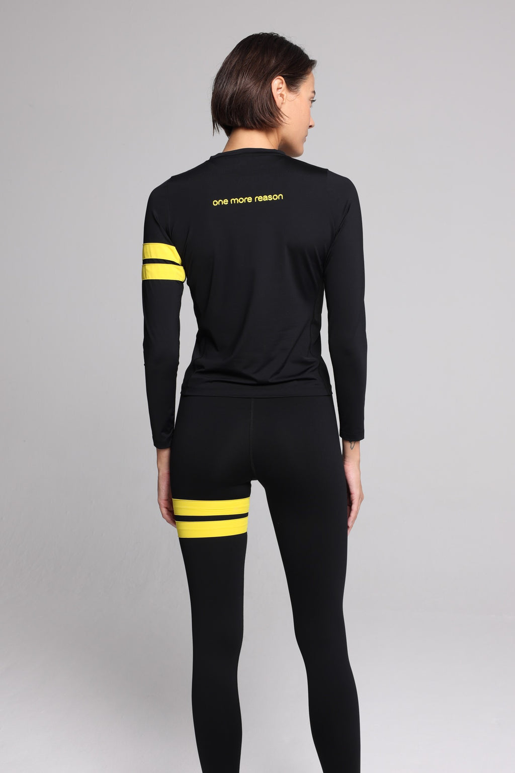women in black long sleeve performance top with yellow stripes top premium luxury activewear by One More Reason high-performance fitness apparel back view